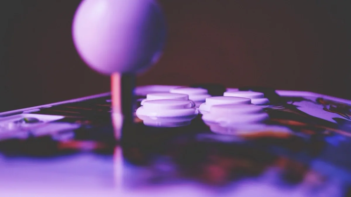 Close-up of an arcade fight stick's ball-top lever and white face buttons lit in purple