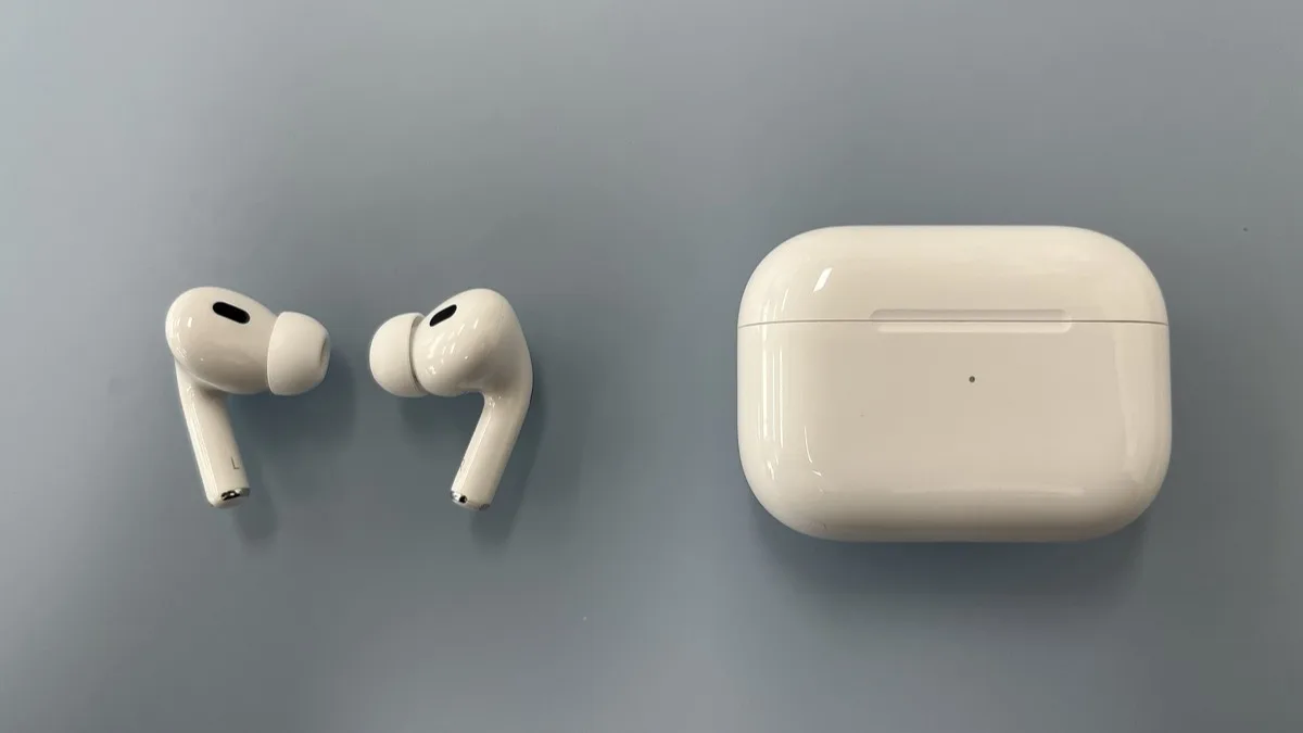 A pair of white AirPods Pro earbuds next to their charging case on a grey surface
