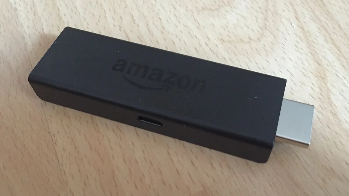 An Amazon Fire TV Stick resting on a wooden table, showing its HDMI connector
