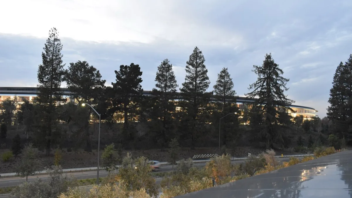 Apple Park in Cupertino, California, the headquarters of Apple, seen at dusk behind a line of trees