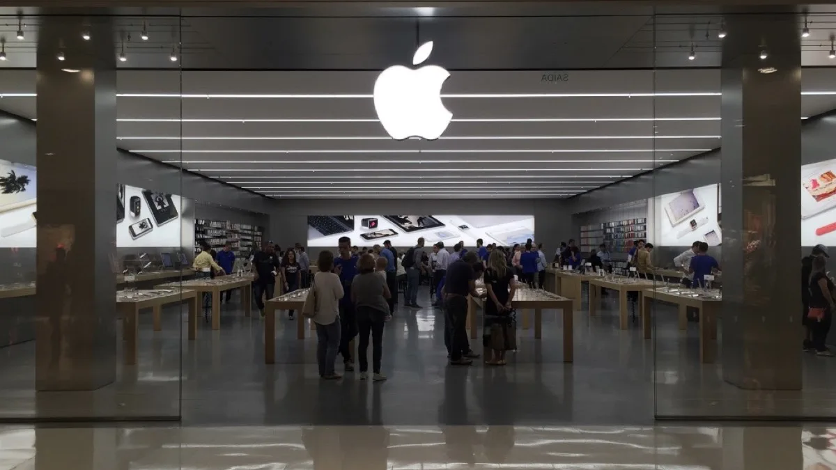 Shoppers browsing product tables inside an Apple Store in Brazil, seen through the storefront glass