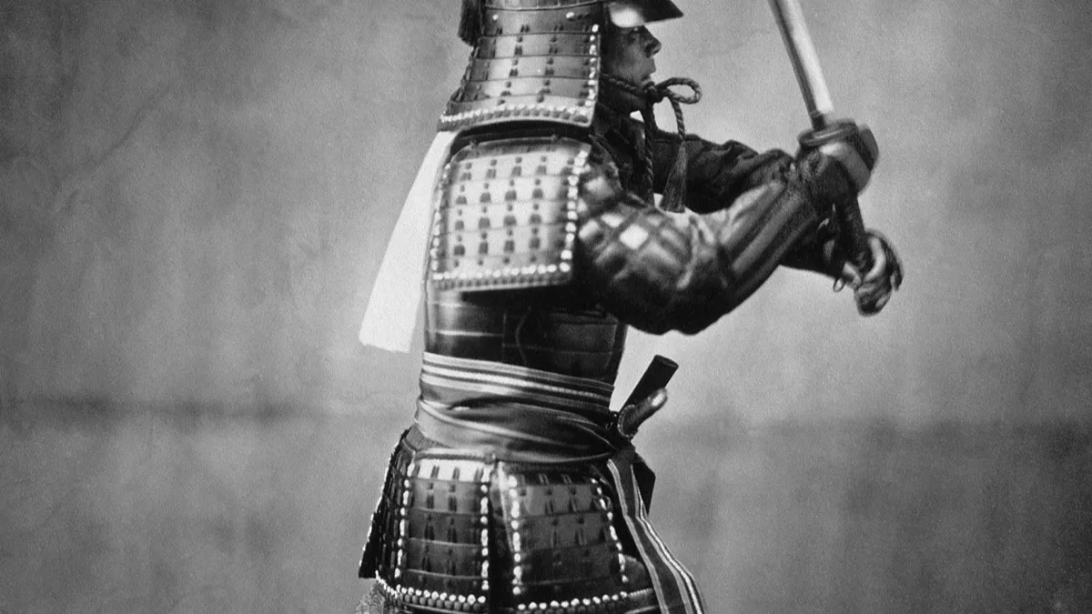 A historical black-and-white photograph of a samurai in full armour raising a drawn sword