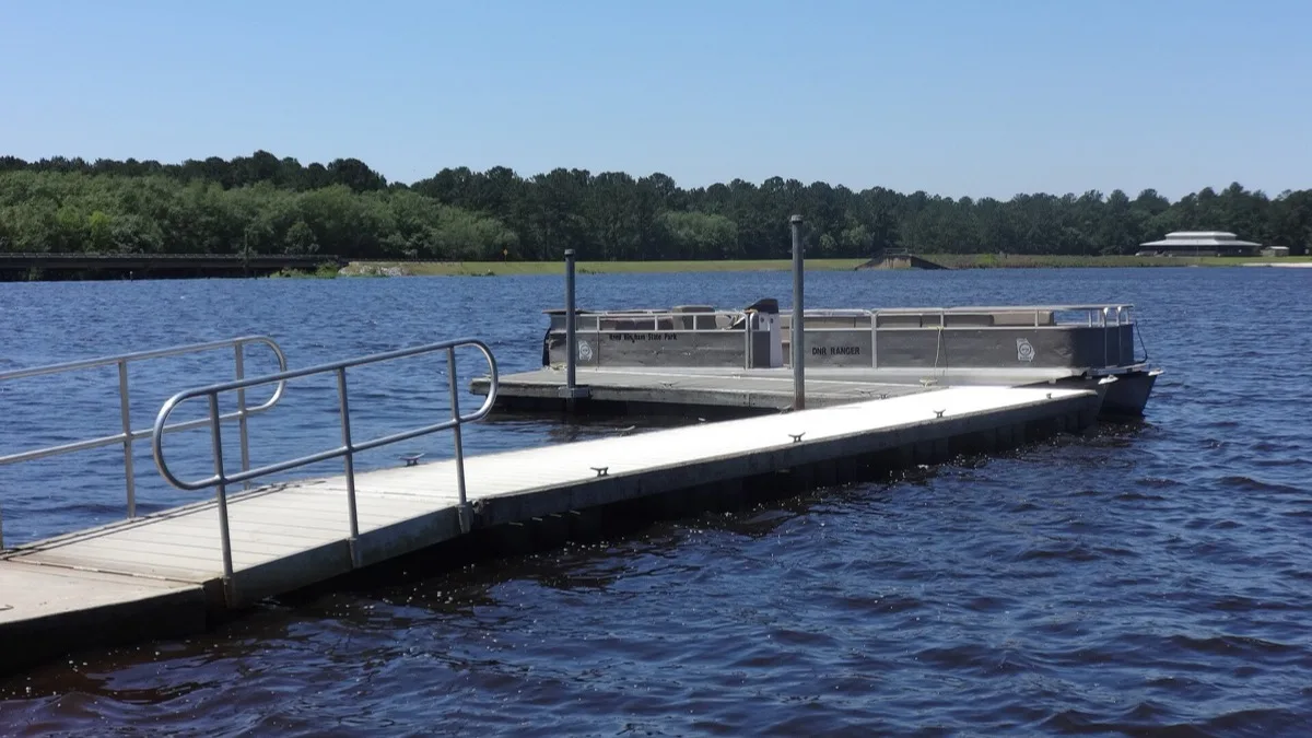 A pontoon boat moored alongside a floating dock on a lake under clear skies