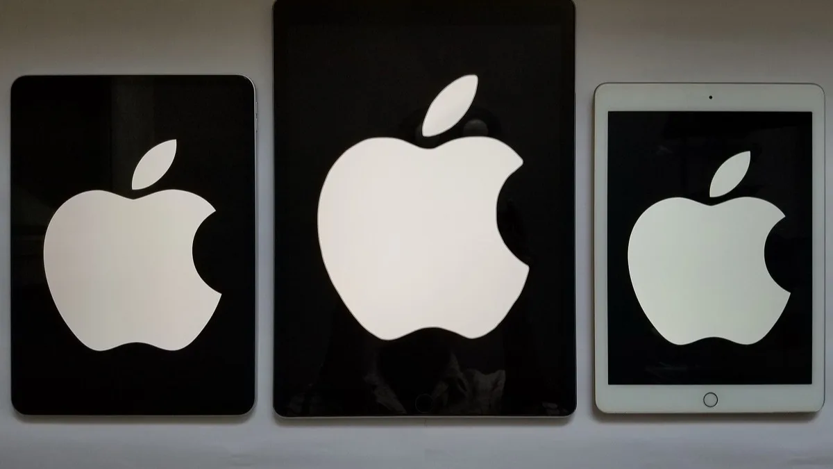 Three iPad models of different sizes standing side by side with the Apple logo lit on their screens