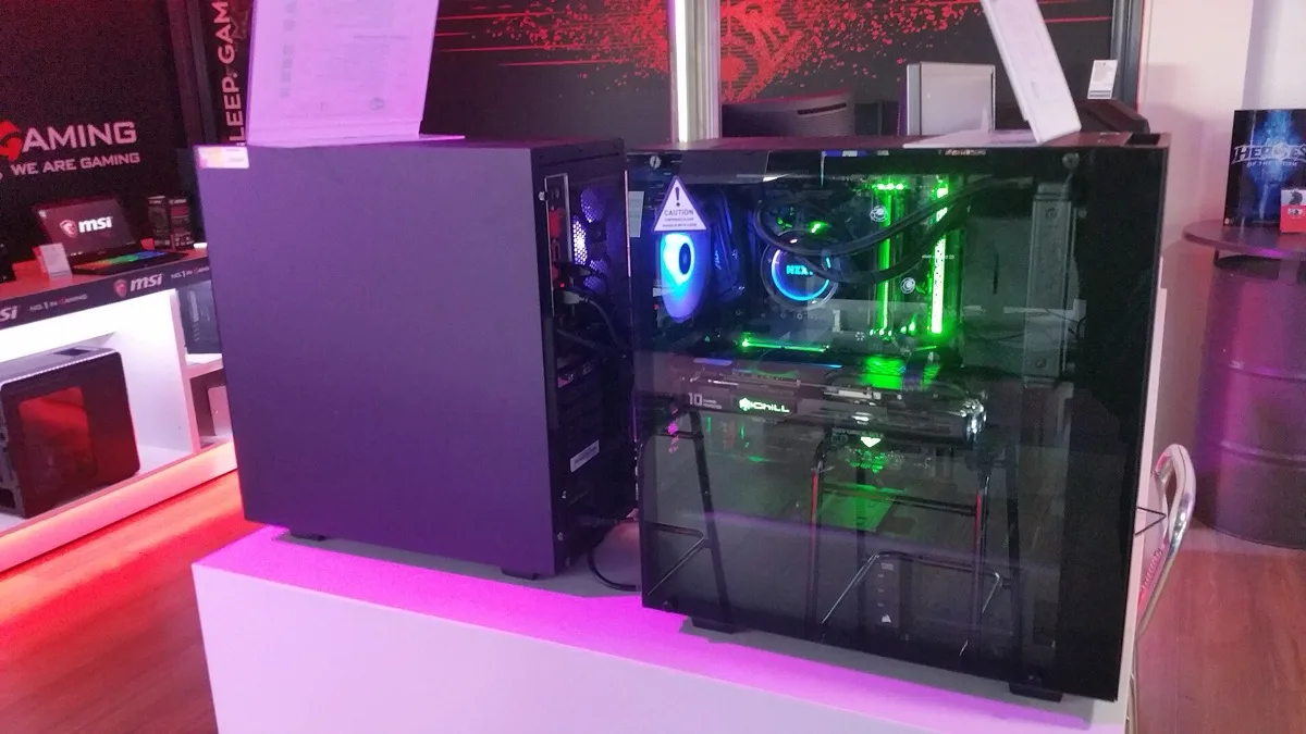 A liquid-cooled gaming PC with a glass side panel and green interior lighting on display beside a second tower