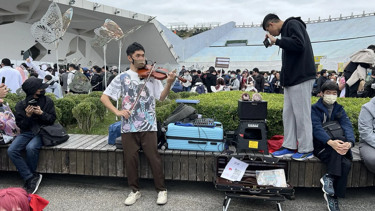 A street violinist performs outdoors at a crowded event while onlookers film him on their phones
