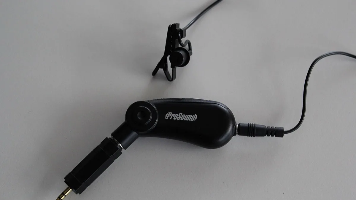 A black clip-on lavalier microphone with its cable and connector laid out on a grey surface