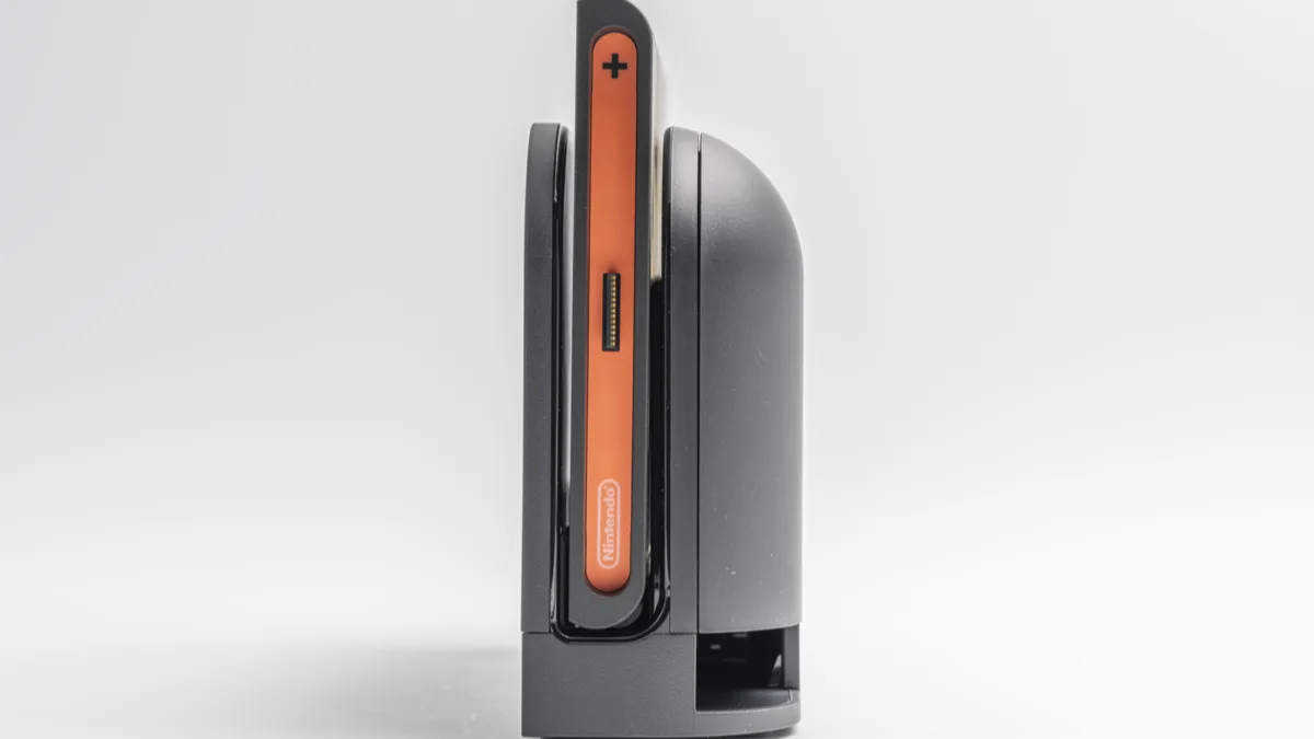 A Nintendo Switch 2 console seen edge-on in its dock, with the orange Joy-Con rail and Nintendo logo facing the camera