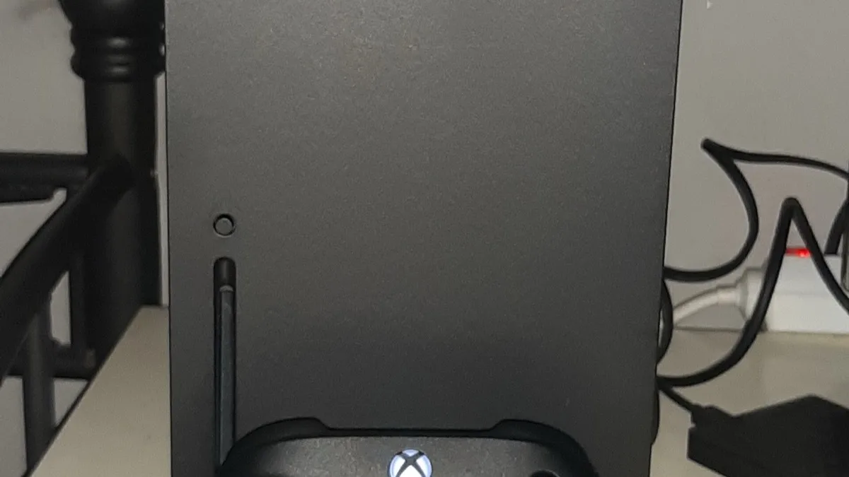 A black Xbox Series X console standing upright on a desk with a matching wireless controller resting in front of it