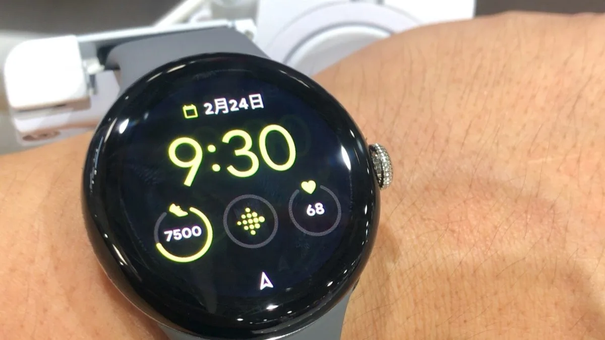 A Google Pixel Watch worn on a wrist, showing its round watch face with time, date, and fitness rings