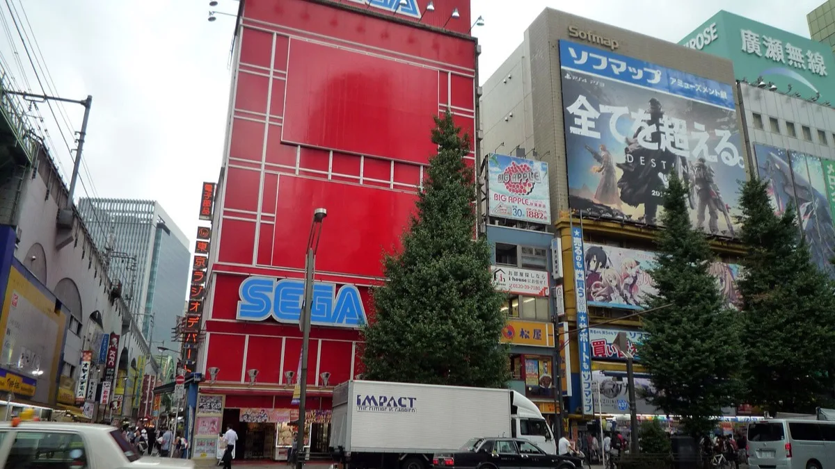 A red Sega arcade building on a busy Akihabara street in Tokyo, surrounded by game shops and advertising boards