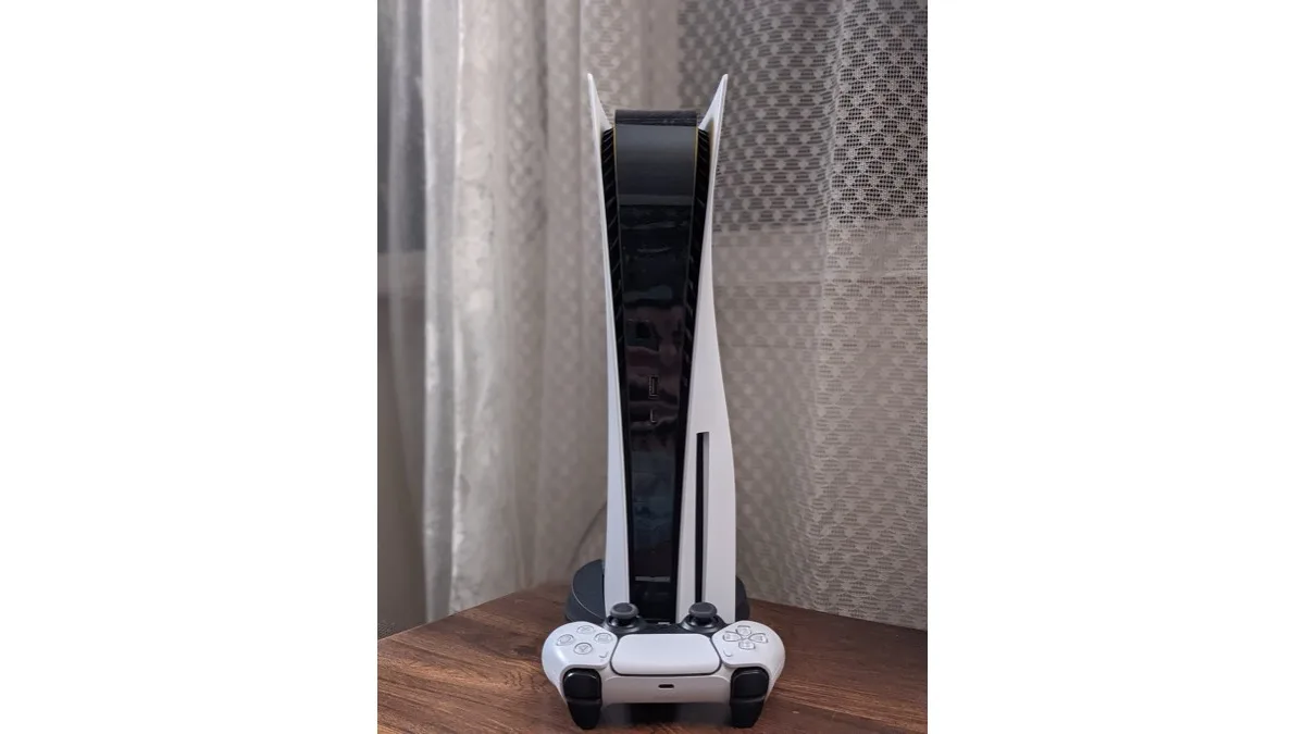 A white PlayStation 5 console standing upright on a wooden table with a DualSense controller in front of it