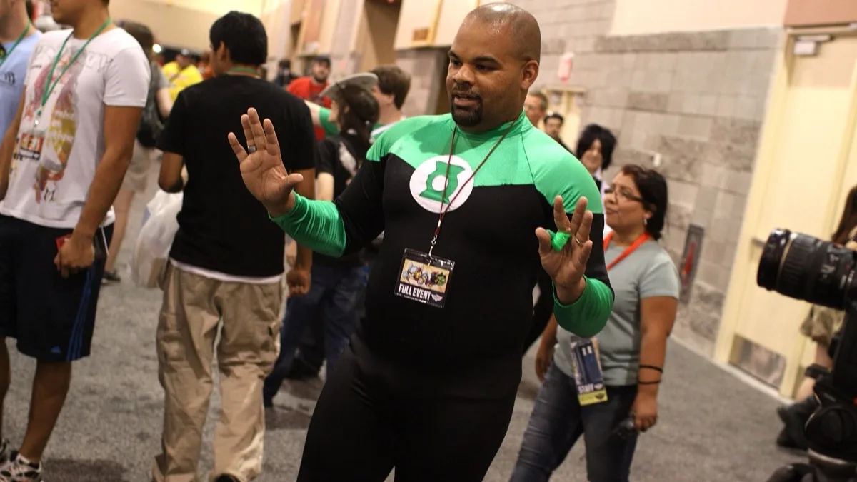 A fan in a Green Lantern costume walking through a convention hall past other attendees