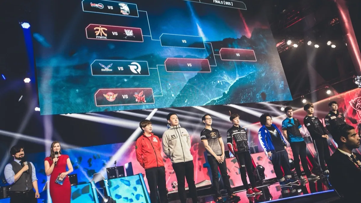 Esports teams stand on a brightly lit stage in front of a large tournament bracket screen at a League of Legends World Championship event