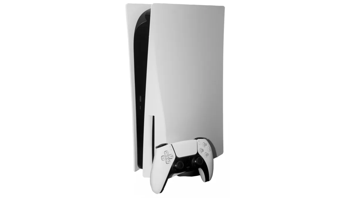 A white PlayStation 5 console standing upright beside its white DualSense controller on a plain background