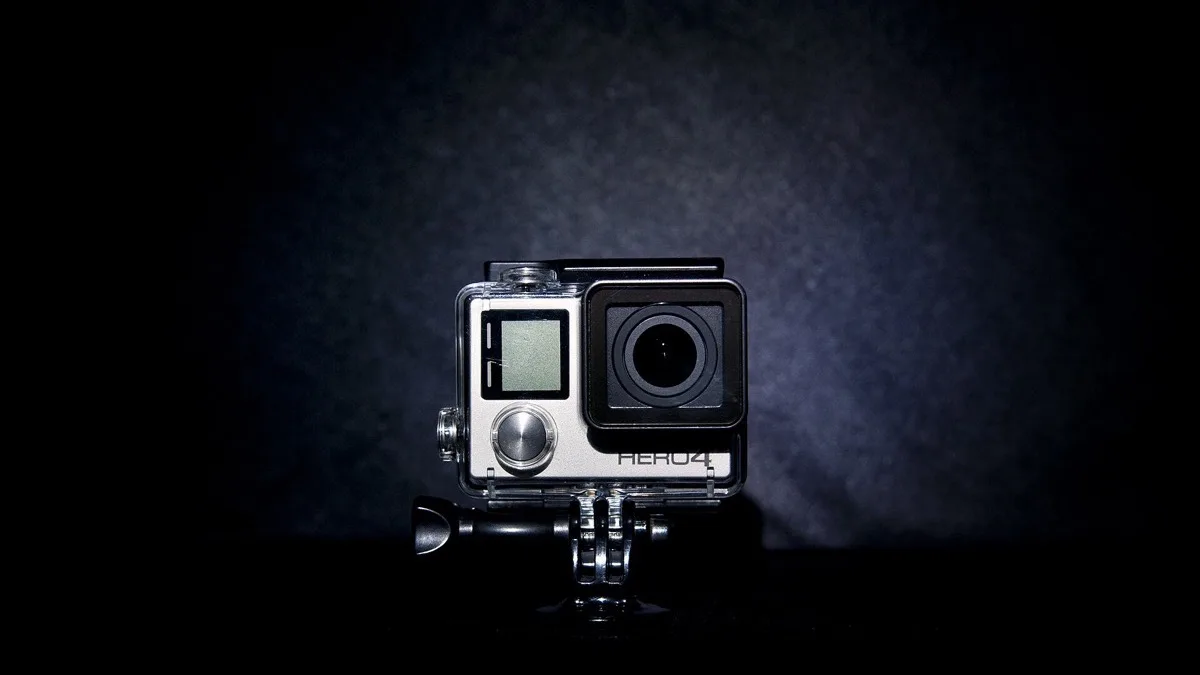 A GoPro Hero action camera in a clear waterproof housing, mounted on a tripod adapter against a dark background