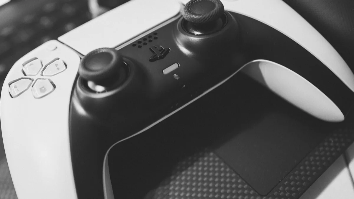 Close-up black-and-white photograph of a PlayStation 5 DualSense controller resting on a desk