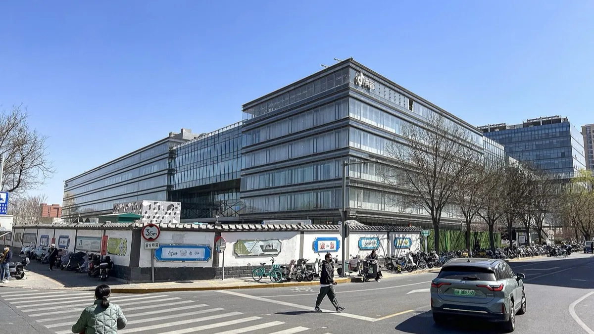 A glass-fronted ByteDance office building on a city street corner with parked scooters and pedestrians
