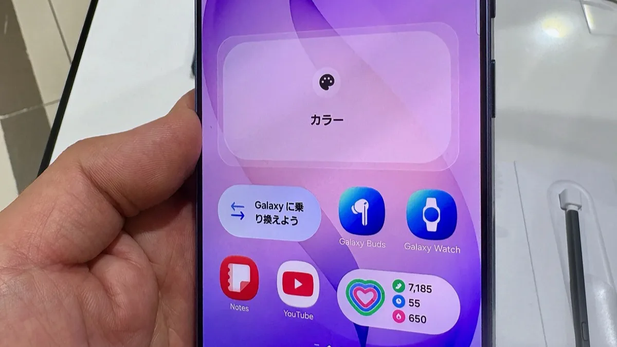 A hand holding a Galaxy S26 series phone showing its home screen with Galaxy Buds, Galaxy Watch and health widgets