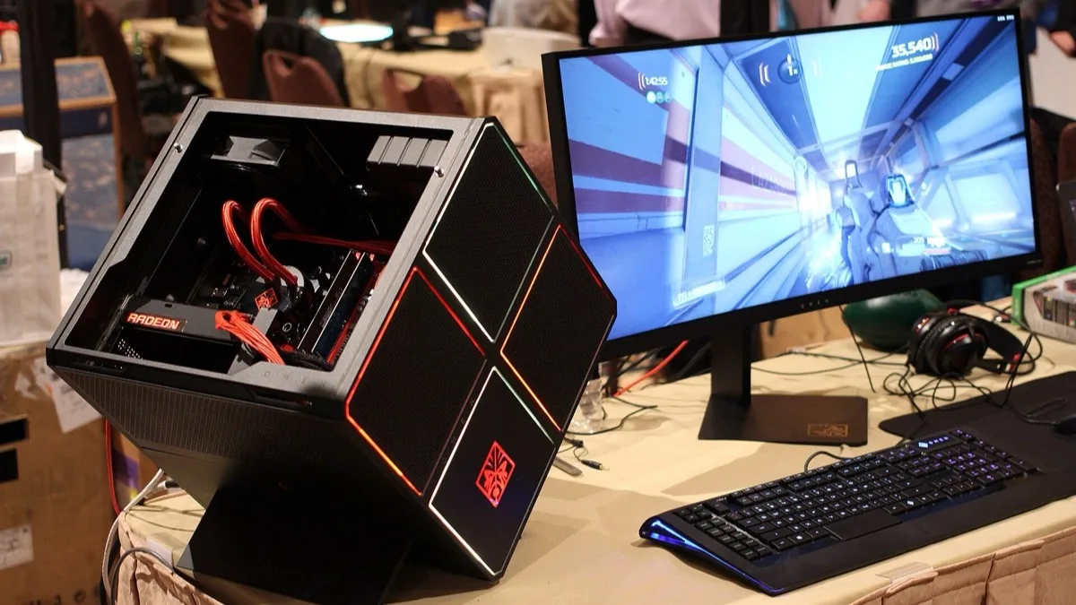 An HP Omen X gaming desktop with a Radeon graphics card on display beside a monitor running a first-person shooter