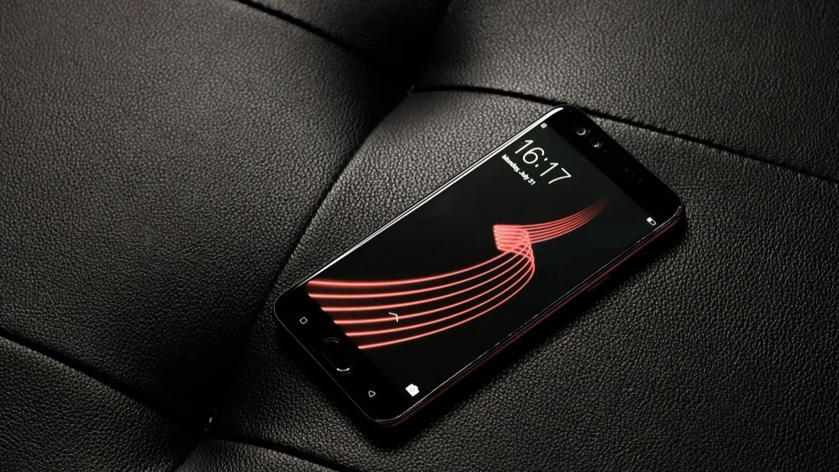 An Oppo smartphone lying face up on a dark leather seat, screen showing a red abstract wallpaper