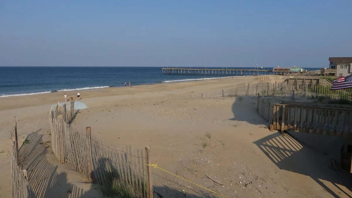 A wide sandy beach with dune fencing and a fishing pier on the Atlantic shore at Nags Head, North Carolina