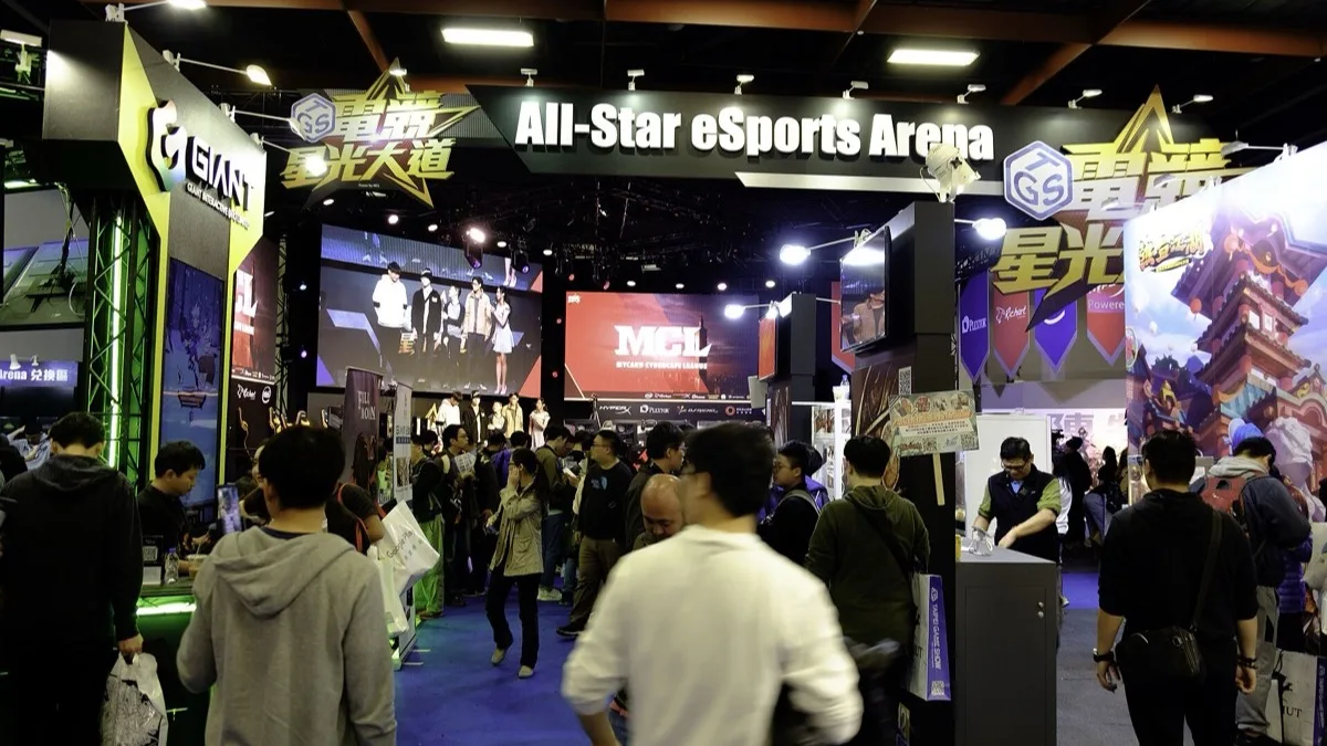 Visitors crowd the All-Star eSports Arena stand at a games trade show, with match screens mounted overhead
