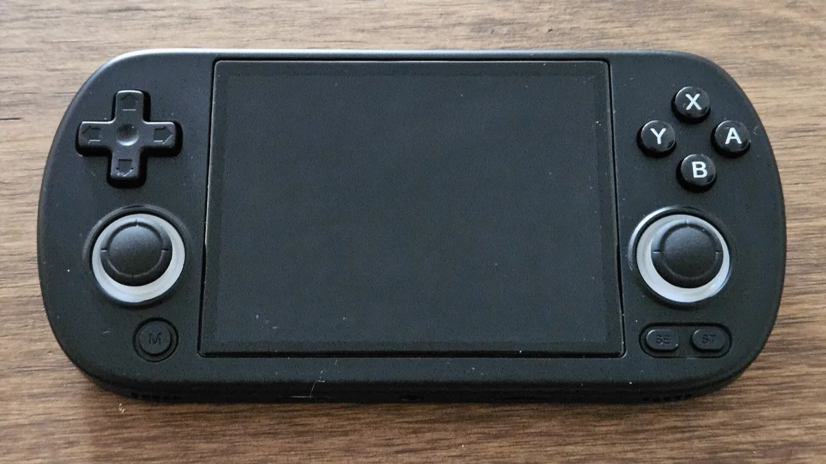 A black Android retro gaming handheld with a d-pad, dual analogue sticks and face buttons, resting on a wooden desk