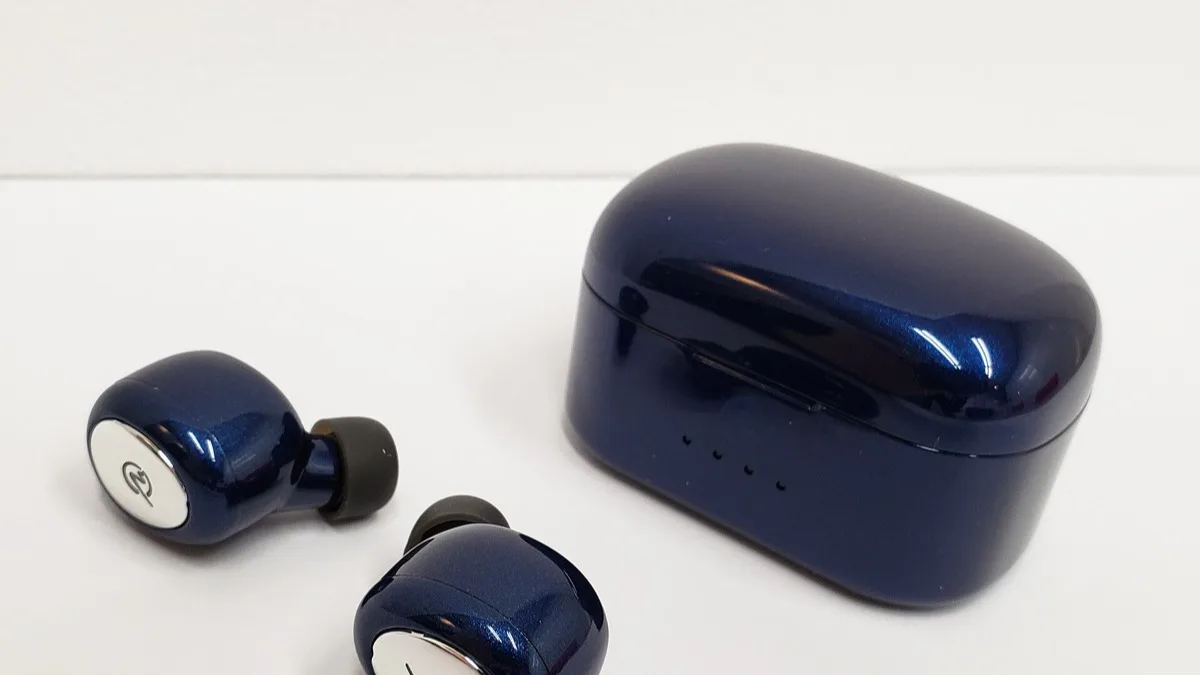 A pair of true wireless earbuds resting beside their open charging case on a white surface