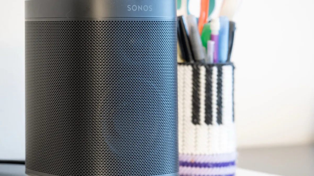 A black Sonos One speaker on a desk next to a pen holder