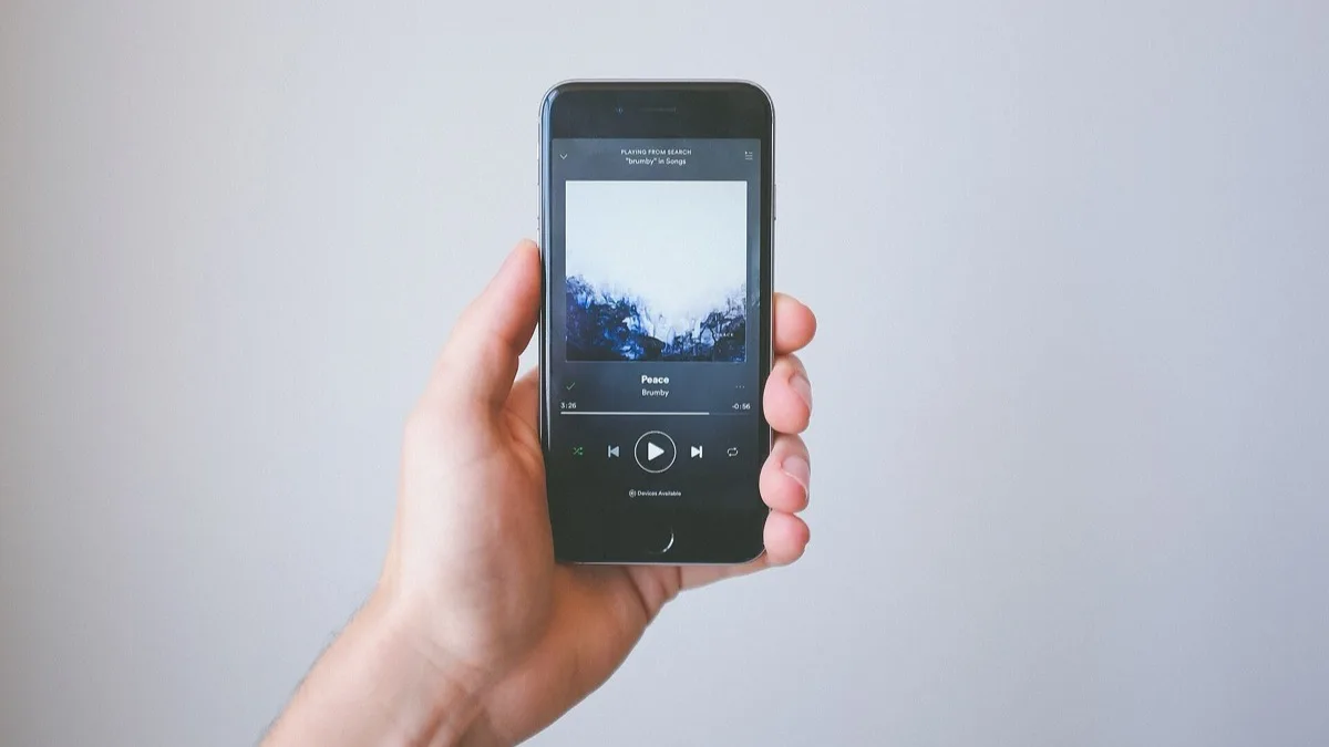 A hand holding a smartphone with the Spotify player open on a track