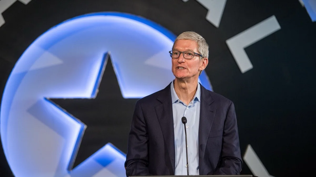 Tim Cook speaking at a podium in a dark suit and light blue shirt