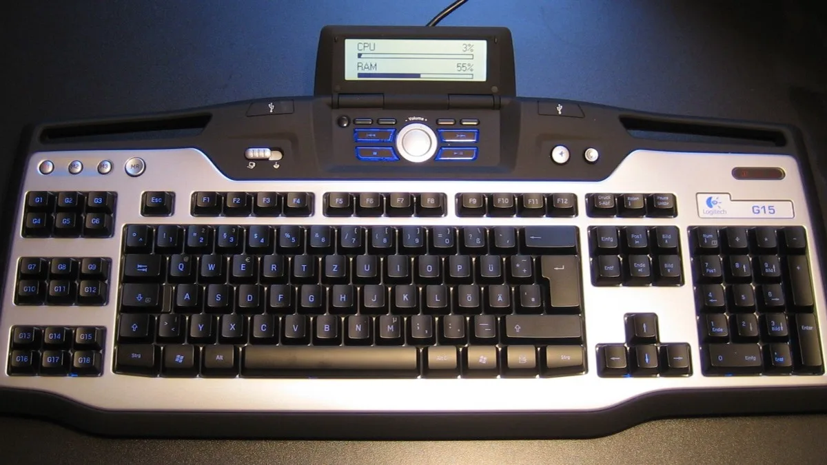 A Logitech G15 gaming keyboard with blue backlighting and a small LCD panel showing CPU and RAM usage, photographed from above on a desk