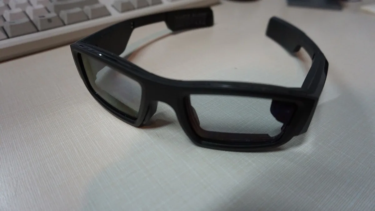 A pair of black wearable display glasses resting on a desk beside a keyboard