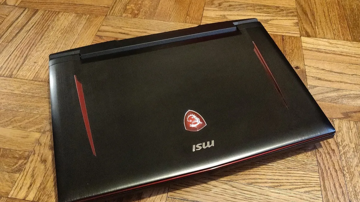 A closed black MSI gaming laptop with red trim resting on a wooden floor