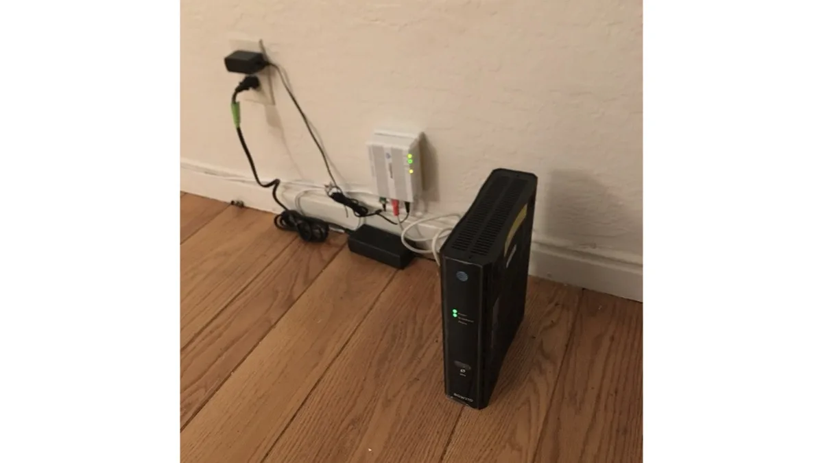 A home cable modem and Wi-Fi gateway connected to a wall outlet on a wood floor