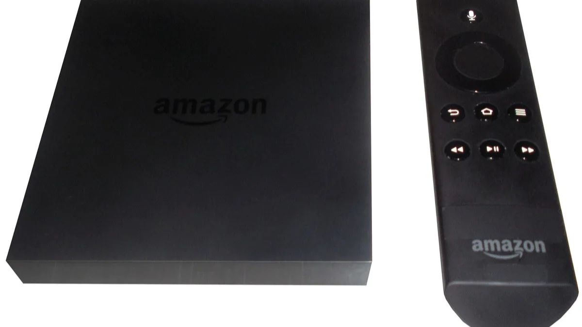 A black Amazon Fire TV streaming box sitting beside its voice remote on a white surface