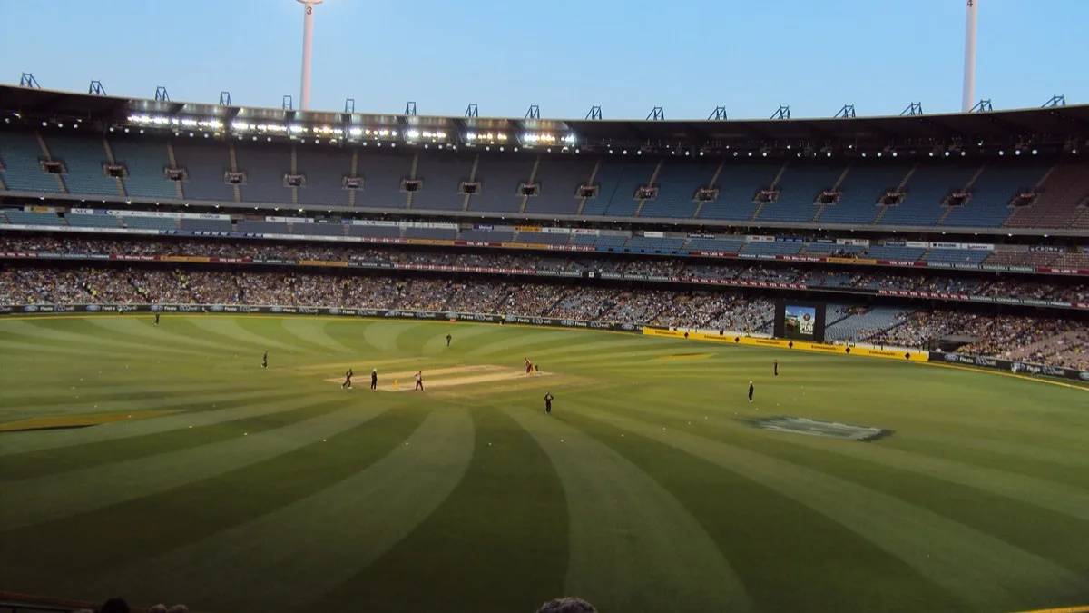 The Melbourne Cricket Ground bowl under floodlights during a cricket match, with the striped playing surface and packed lower stands in view