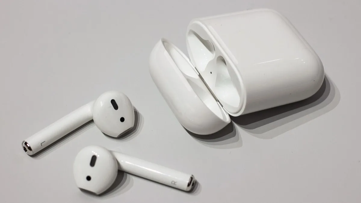 Open-ear Apple AirPods lying beside an open charging case on a white surface