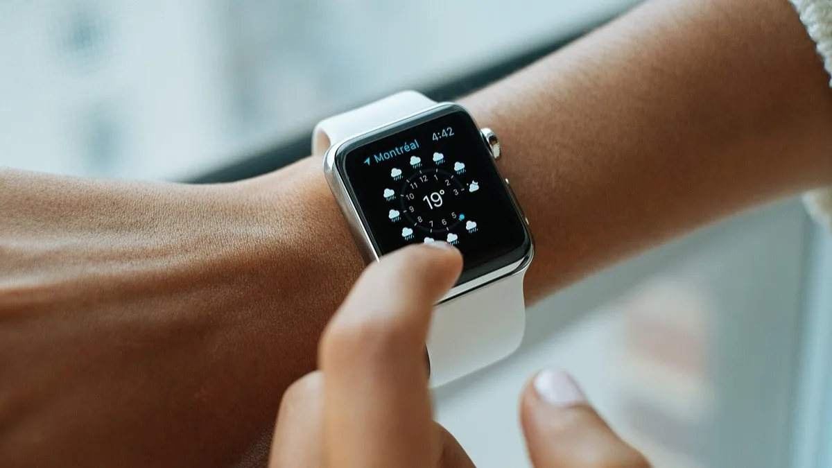 Apple Watch worn on a wrist, with a finger tapping the weather complication on the display