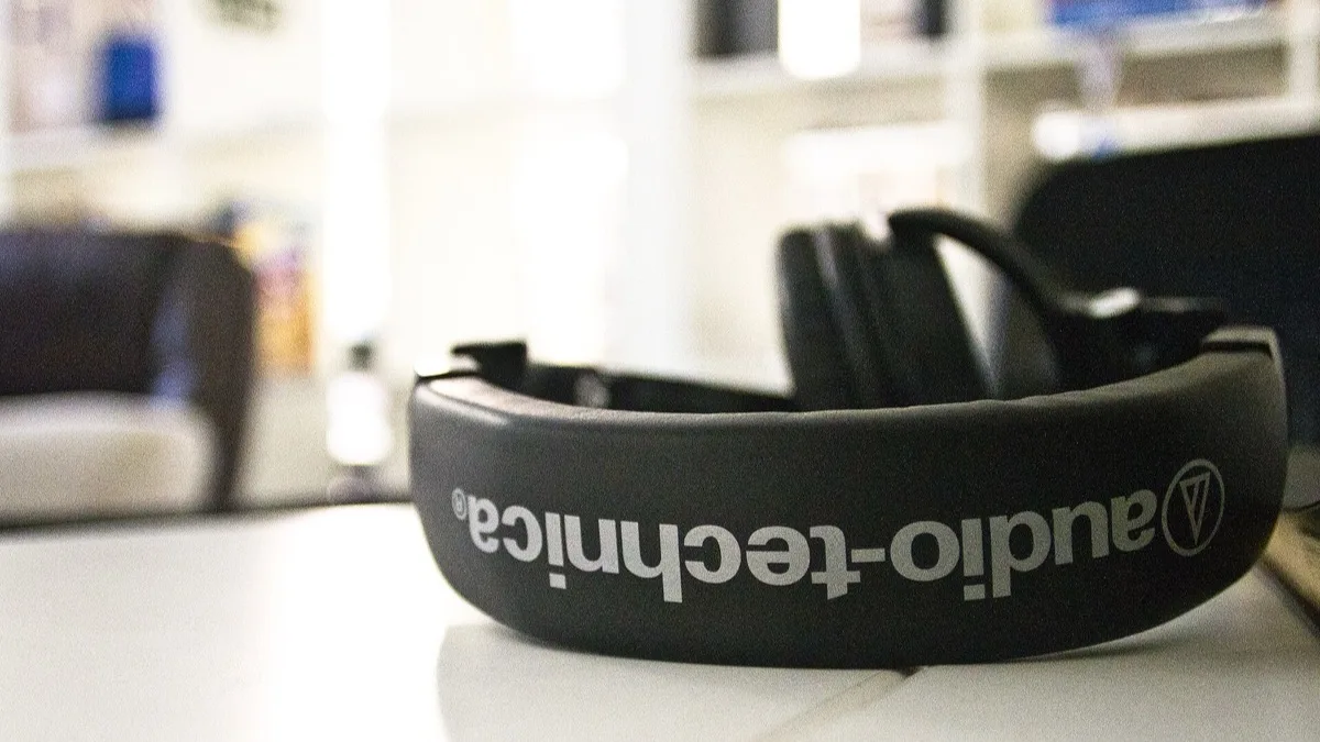 Audio-Technica over-ear headphones resting on a white desk with the brand name visible on the headband