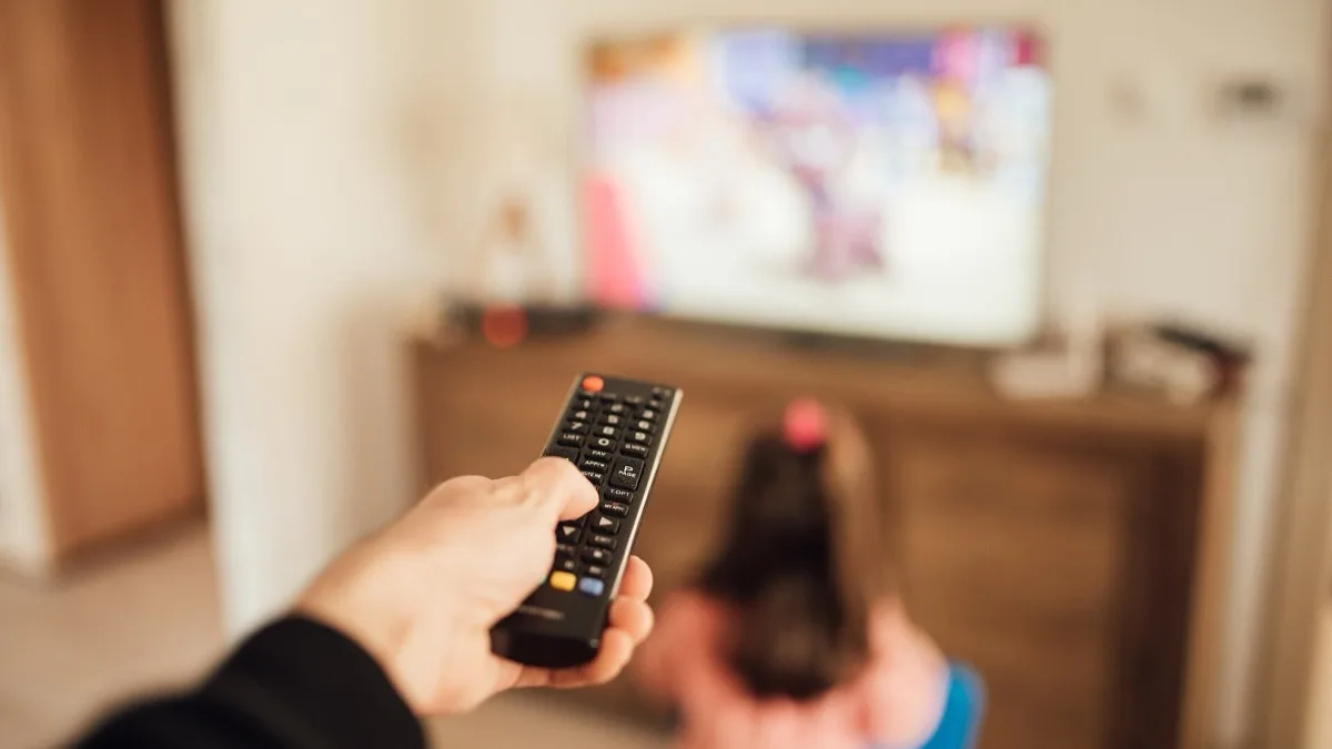 A hand pointing a black remote control at a wall-mounted television in a living room