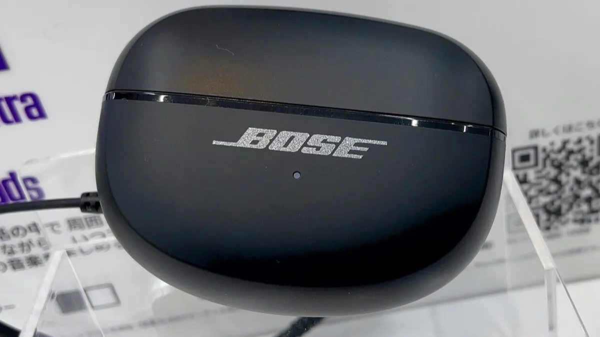 Black charging case of the first-generation Bose Ultra Open Earbuds on a retail display stand