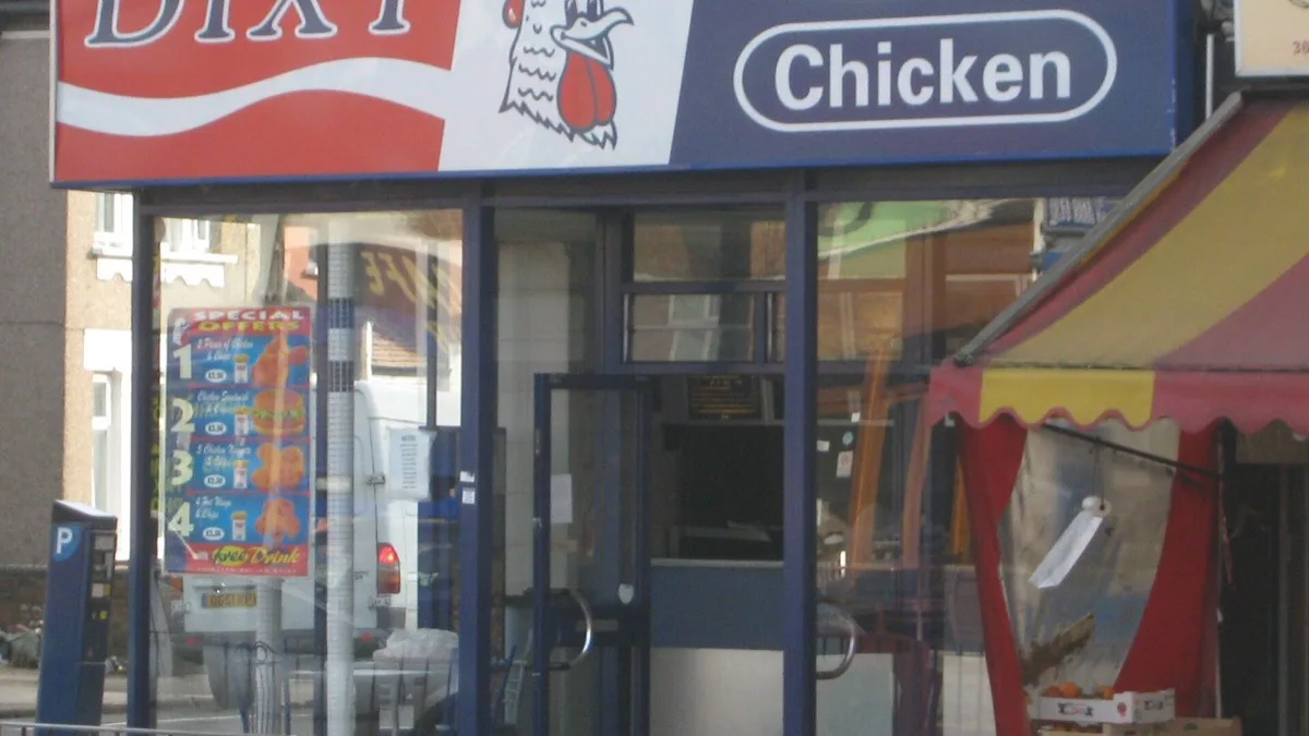 The frontage of a Dixy Chicken fried chicken shop on a London high street, with a special offers poster in the window