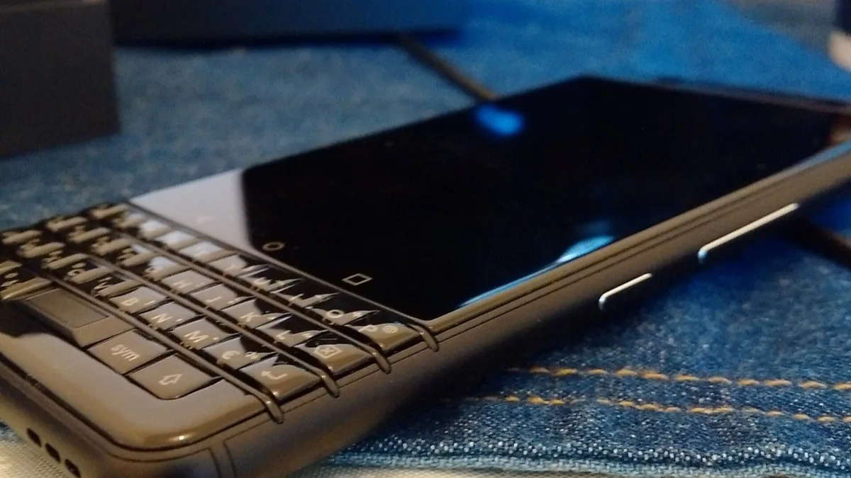 Close-up of a black BlackBerry KEYone phone with its physical QWERTY keyboard, lying on denim