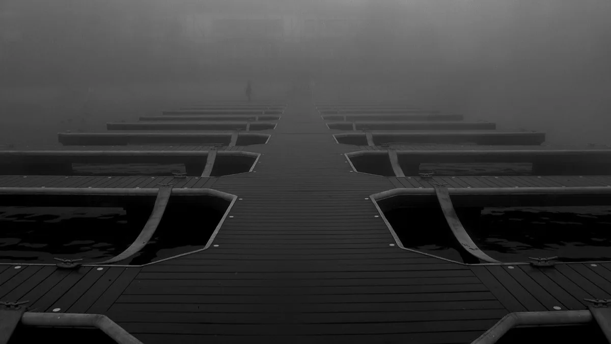 A black-and-white photo of an empty boat dock stretching into thick fog on Lake Arrowhead, California