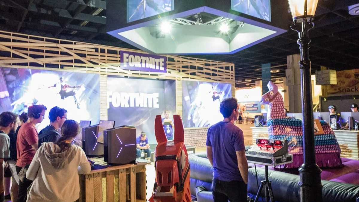 Visitors playing Fortnite on gaming PCs at the Fortnite booth at Gamescom 2017, with a large Loot Llama pinata beside them