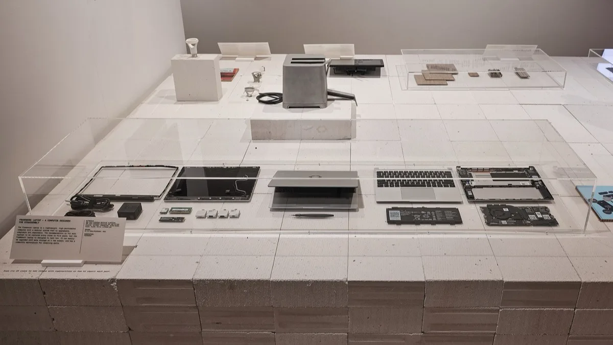 A Framework Laptop broken down into its display, keyboard deck, mainboard, battery and expansion cards, laid out in a museum display case