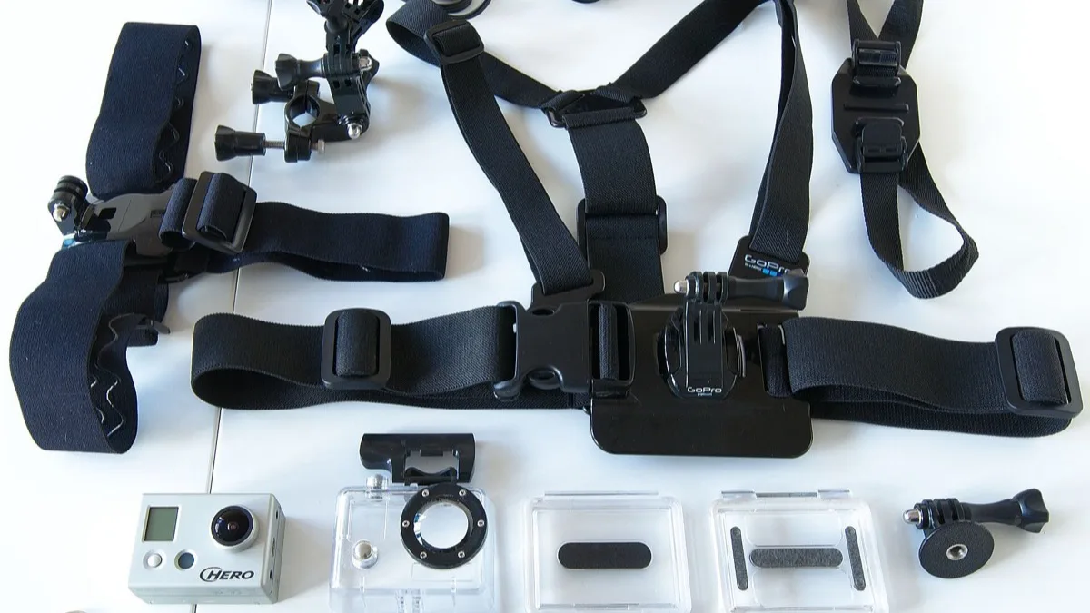 A GoPro action camera laid out on a white surface with its chest harness, head strap, waterproof housings and mount adapters