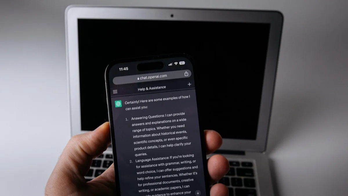 ChatGPT running in a phone browser held in front of a laptop, illustrating OpenAI's consumer chat app